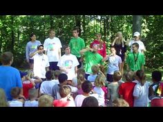 a group of young people standing around each other in front of a tree filled forest