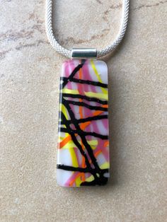 This is a fun fused glass pendant necklace, with opalescent in pink, white, black, yellow and orange. The pendant is approximately .75" x 1.75" and  comes on a 16" mesh choker with lobster clasp. Other pieces available separately.  Caring for fused glass jewelry: To clean, use a soft cloth. Do not use harsh chemicals to clean. Should not be submerged in water, and should be removed when bathing. While fused glass is much stronger, use care when handling as can still break if dropped on hard surface.  Please contact me with any questions, changes or modifications.  Thank you so much for stopping at my shop! Fused Glass Pendant Necklace, Fused Glass Necklace, Art Glass Jewelry, Glass Fusion Ideas, Fused Glass Artwork, Glass Craft, Glass Fusion, Fused Glass Pendant, Fused Glass Jewelry