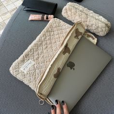 a person is holding an apple laptop on a table with other items around it and the cover has been opened