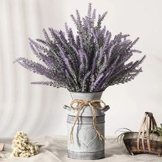 purple flowers are in an old tin can with twine handles and ribbon tied around the top