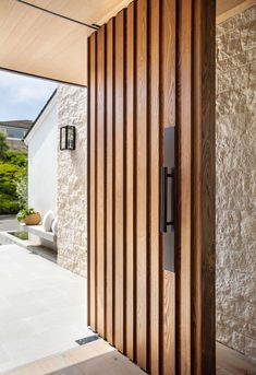 an open door with wooden slats in front of a white house and stone wall