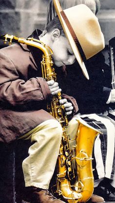 a young boy sitting on the ground next to a yellow saxophone and wearing a hat