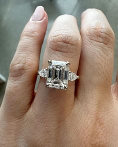 a woman's hand holding an engagement ring with three stones on it and the center stone is surrounded by smaller diamonds