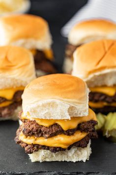 three cheeseburger sliders with pickles on the side, ready to be eaten