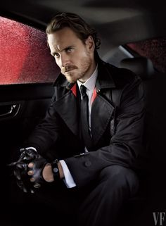 a man in a suit and tie sitting in a car with his hands on the steering wheel