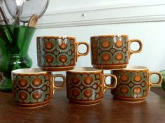 six coffee cups sitting on top of a wooden table next to a vase with flowers in it