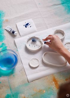 a person is painting on a table with blue and white paint in the process of making bowls