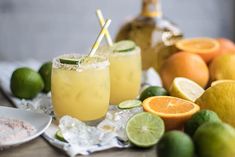 two glasses filled with lemonade next to limes and oranges