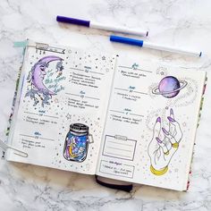 an open notebook with drawings on it next to a pen and marker, surrounded by space related items