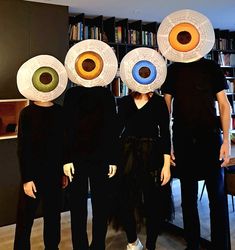 three people standing in front of bookshelves with paper plates on their heads and eyes