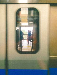 two people standing on a subway platform looking out the window