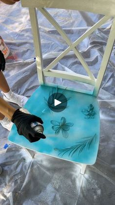 a person painting a chair with blue paint and black gloves on the ground next to it