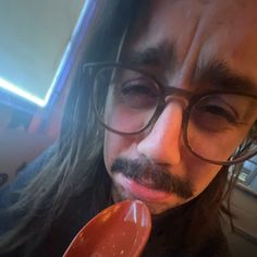 a man with long hair and glasses is holding a spoon in his hand while looking at the camera