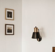 a black lamp hanging from the side of a white wall next to a wooden table