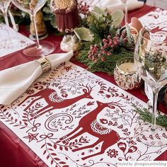 a table topped with glasses and plates covered in red cloths next to christmas decorations