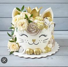 a white cat cake with gold decorations and flowers on the top is sitting on a table