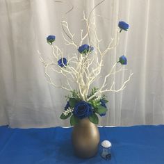 a vase filled with blue flowers on top of a blue tablecloth covered table next to a white curtain