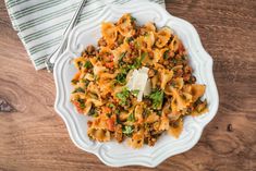 a white bowl filled with pasta and meat on top of a wooden table next to a fork