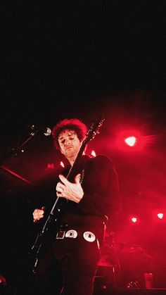 a man holding a guitar while standing in front of a microphone and red light behind him