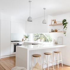 a white kitchen with wooden floors and stools