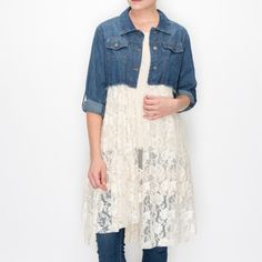 a woman standing in front of a white wall wearing a denim jacket and lace dress