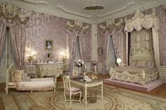 an ornate bedroom with purple walls and curtains on the windowsills is furnished with antique furniture