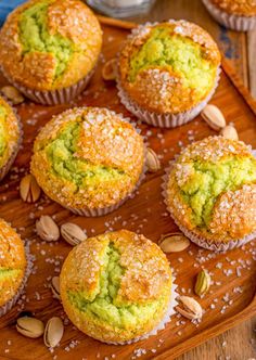 there are many muffins with green toppings on the wooden tray and almonds next to them