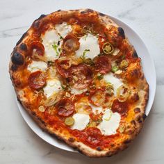 a small pizza on a white plate sitting on a marble counter top next to a fork and knife