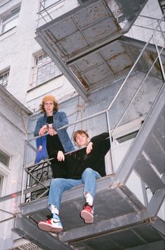 two people sitting on the top of a metal stair case in front of a building