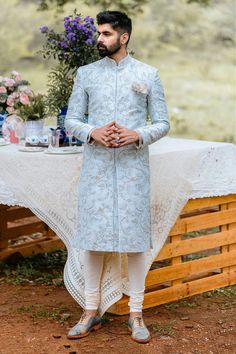 a man standing in front of a table wearing a blue sherve with white pants