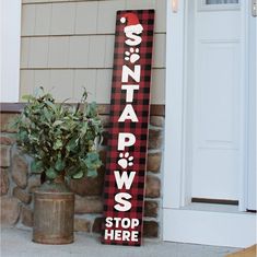 a wooden sign sitting on the side of a building next to a potted plant