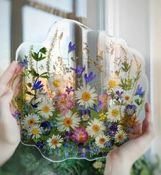 a person holding up a glass plate with flowers on it in front of a window