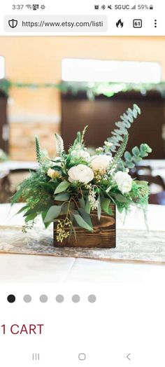 an arrangement of white flowers and greenery in a wooden box on a table at a wedding reception