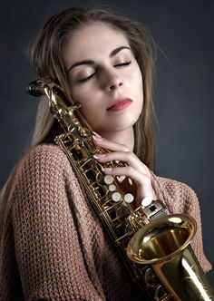 a woman holding a saxophone in her right hand and looking at the camera with eyes closed