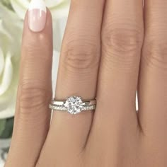 a woman's hand with a diamond ring on it and flowers in the background