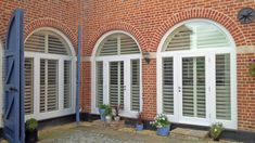 three windows with shutters on the side of a brick building and potted plants