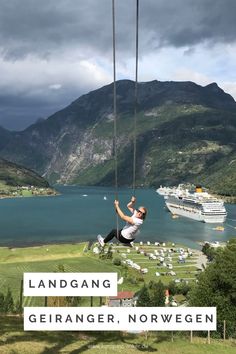 a man is swinging from a rope in front of a large body of water and mountains