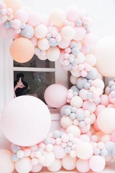 a woman standing in front of a window surrounded by pink, white and grey balloons