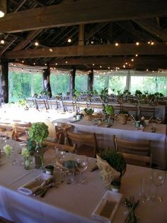 tables set up for an event with white linens and greenery in vases