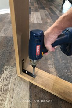 a driller is being used to fix a mirror frame with wood flooring in the background