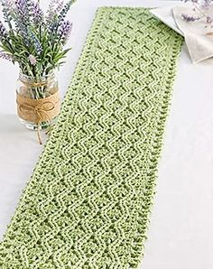 a green crocheted table runner next to a vase with lavenders in it