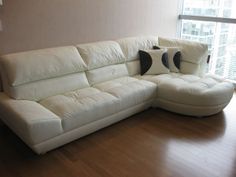 a white leather sectional sofa with pillows on it in front of a large window overlooking the city