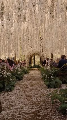 an outdoor ceremony with white flowers and greenery on the ceiling is filled with people