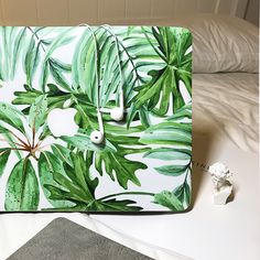 a laptop case with green leaves painted on it and an apple phone next to it