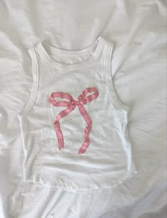 a white tank top with a pink bow on the front and back, sitting on a bed