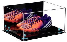 a pair of orange and purple soccer shoes in a clear box with black bottom frame