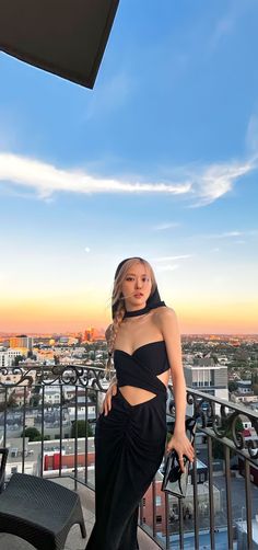 a woman standing on top of a balcony next to a black table and chair in front of a cityscape