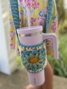 a person holding a coffee cup in their hand with a crocheted flower on it