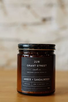 a jar of orange and sandalwood candle on a wooden table with a brick wall in the background