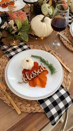 a white plate topped with an orange leaf next to a wine glass and pumpkins